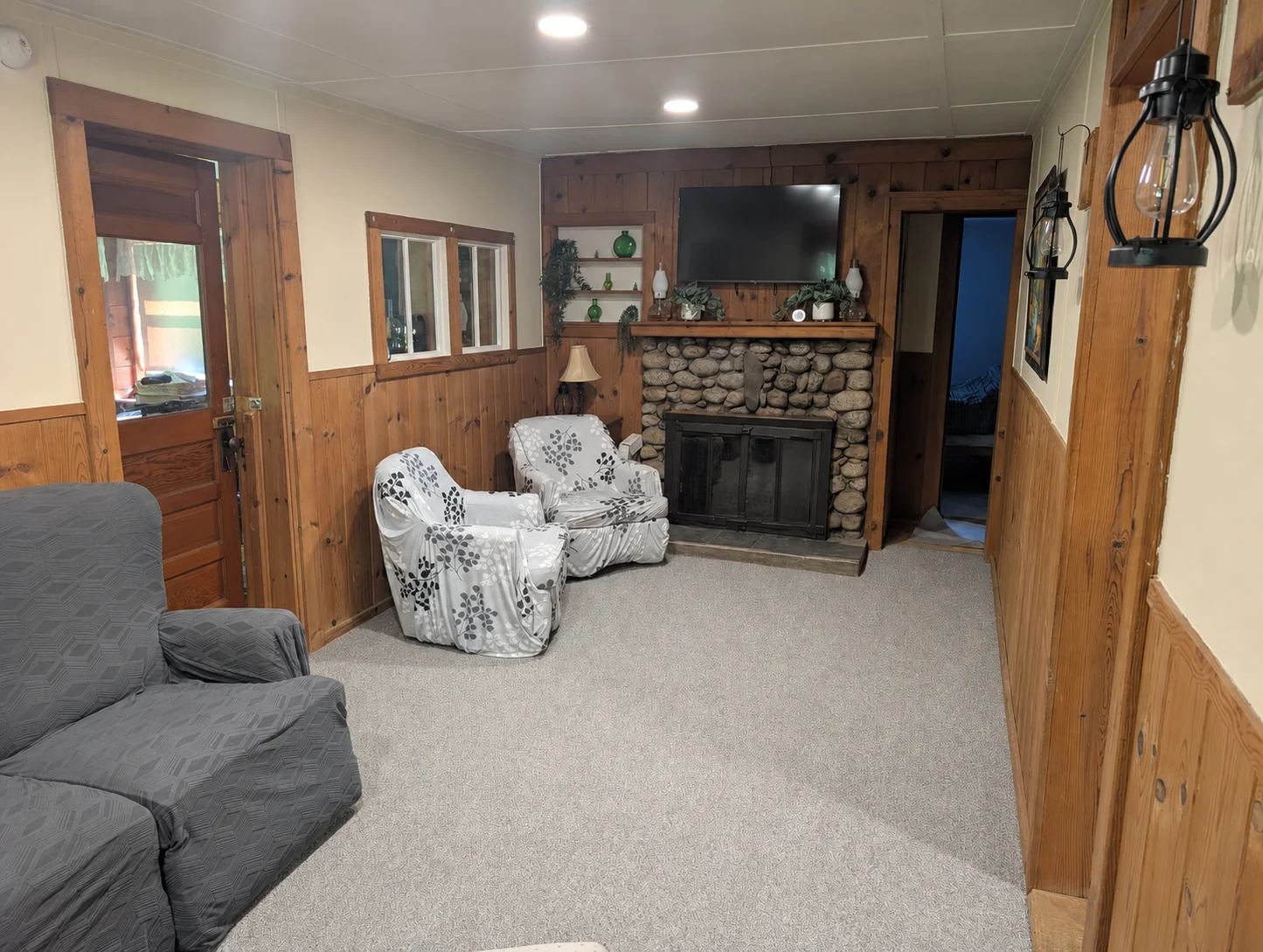 Lounge with a stone fireplace surround, television, armchairs, and wood paneling