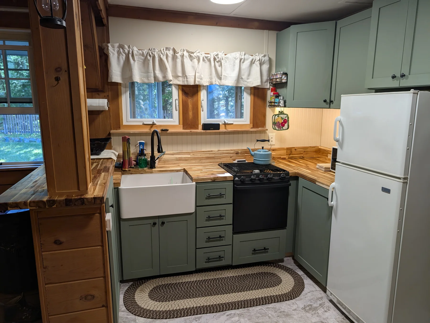 Kitchen with green cabinetry, farmhouse sink, range, refrigerator, and butcher-block counters