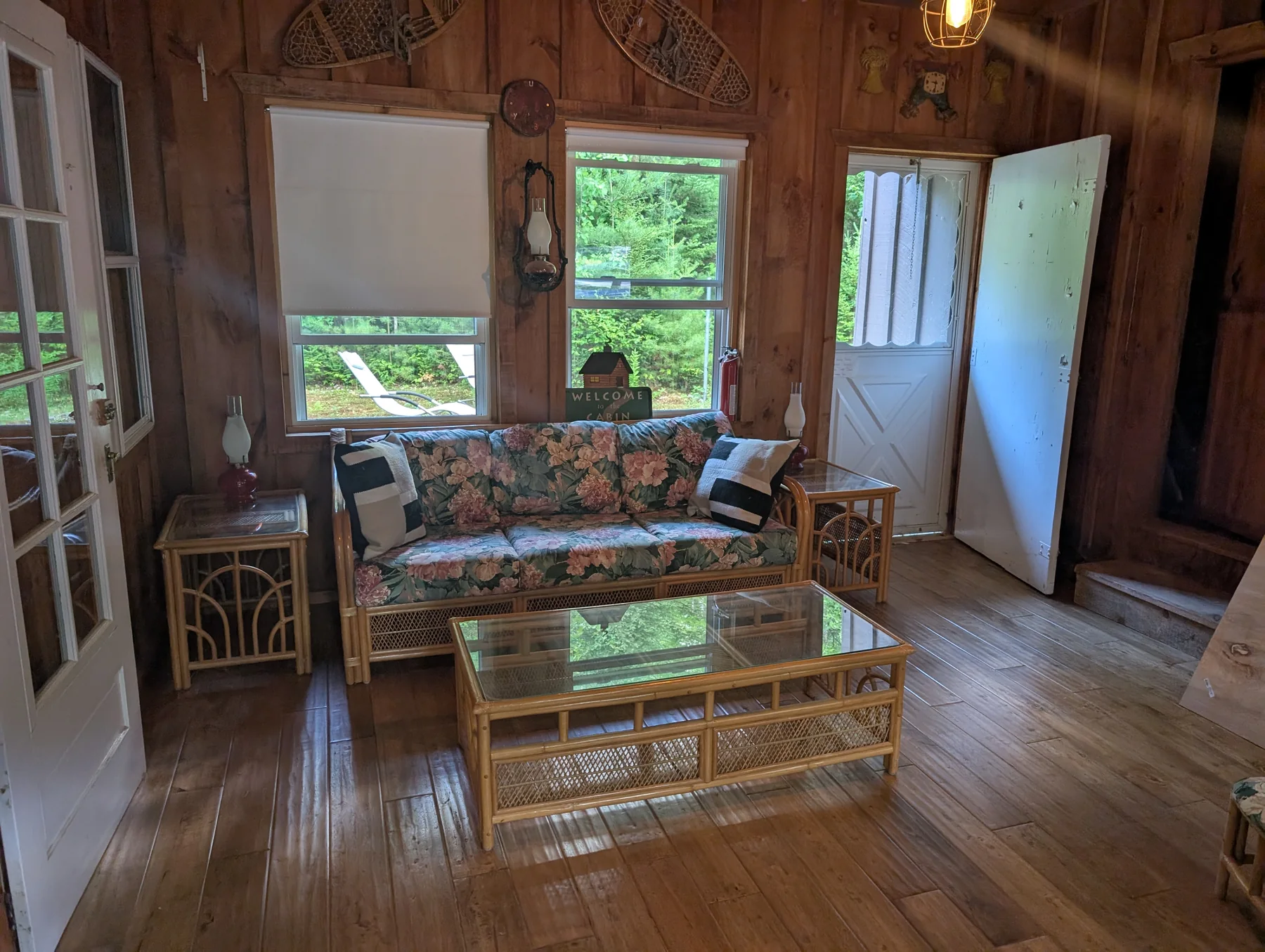 Wood-paneled sitting room with floral sofa, glass coffee table, and open garden door